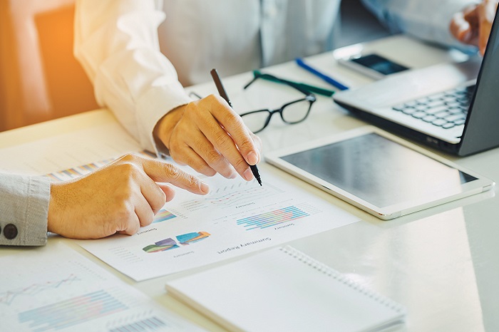 Two businessman analysing company financial report balance sheet statement working with documents graphs.