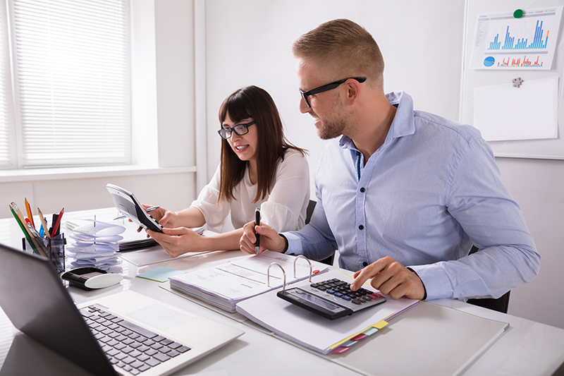 Two employees collaborating and calculating on their devices