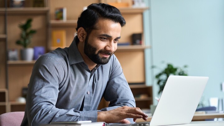 Smiling indian business man working studying on laptop computer at home office