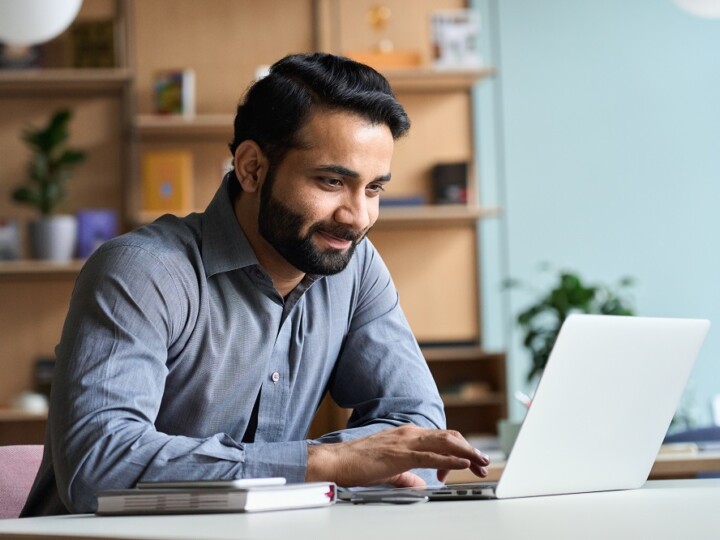 Smiling indian business man working studying on laptop computer at home office