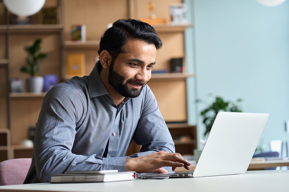 Smiling indian business man working studying on laptop computer at home office