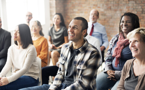 Group of multi-ethnic people sitting in a room all facing the same way, their attention is fixed on What Health and Safety Training in the Workplace Should I Provide?