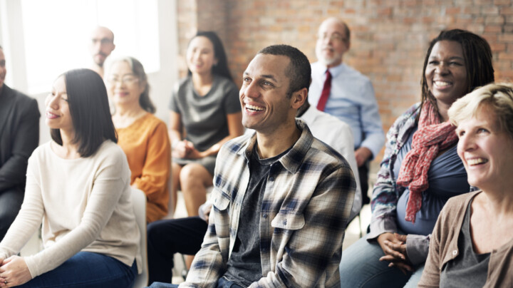 Group of multi-ethnic people sitting in a room all facing the same way, their attention is fixed on What Health and Safety Training in the Workplace Should I Provide?