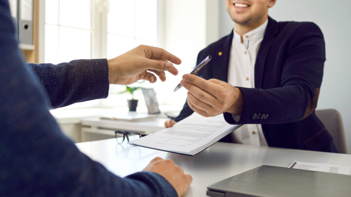 Employee hands over contract and a pen to another employee